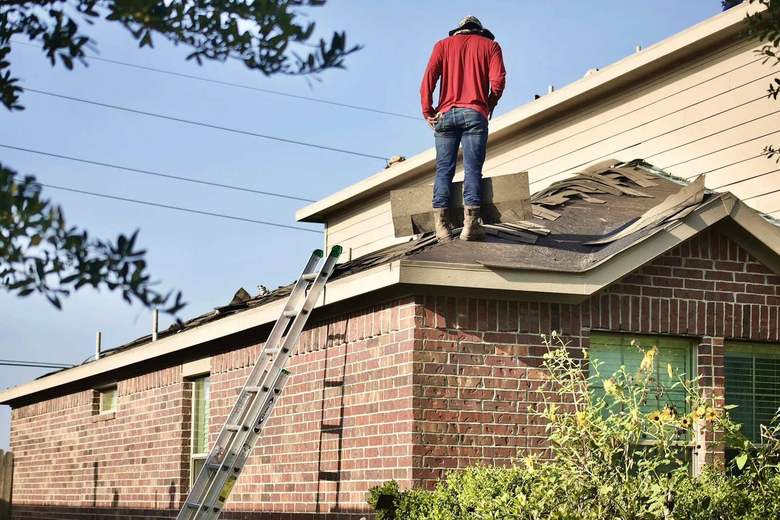 Roofer working on a shingle roof from a ladder